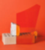 A photograph of a cinder block and piece of clay stacked on top of each other behind a piece of transparent orange plastic, and in front of an orange background of the same hue.